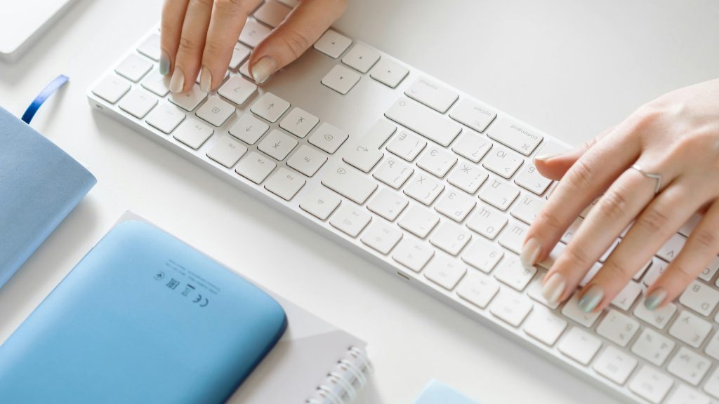 Tastatur mit Händen nd blaueb Büro-Utensilien